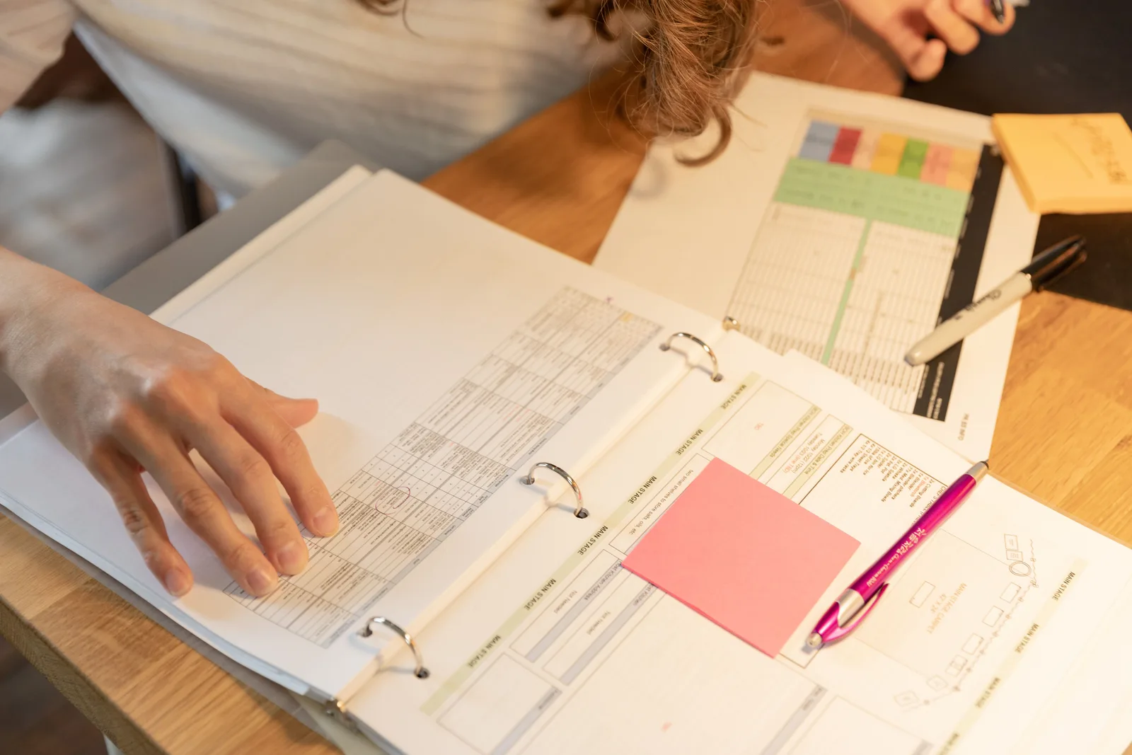 Close-up of an employee sorting documents with sticky notes and pens on a wooden desk. Acquisition financing examples, taken apart