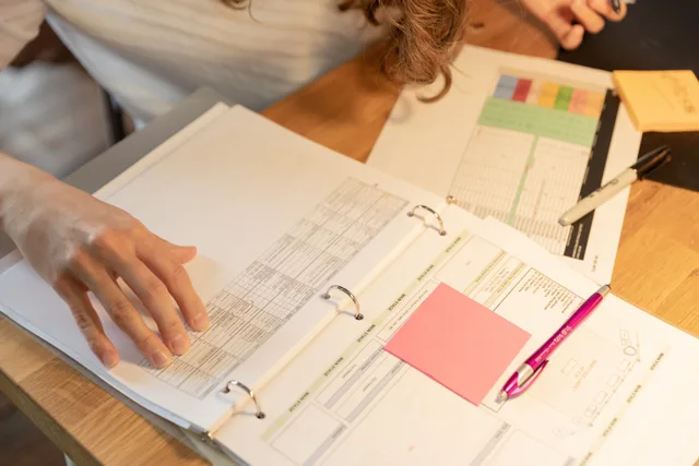 Close-up of an employee sorting documents with sticky notes and pens on a wooden desk. Acquisition financing examples, taken apart
