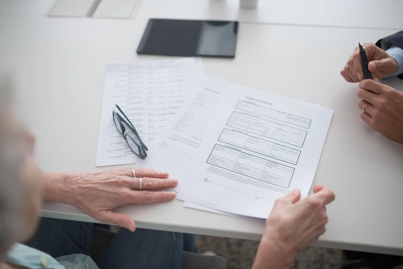 Close-up view of two individuals reviewing documents and forms in an office setting. Acquisition financing structures: SBA 7(a), seller notes, earnouts, mezzanine debt, and who carries risk
