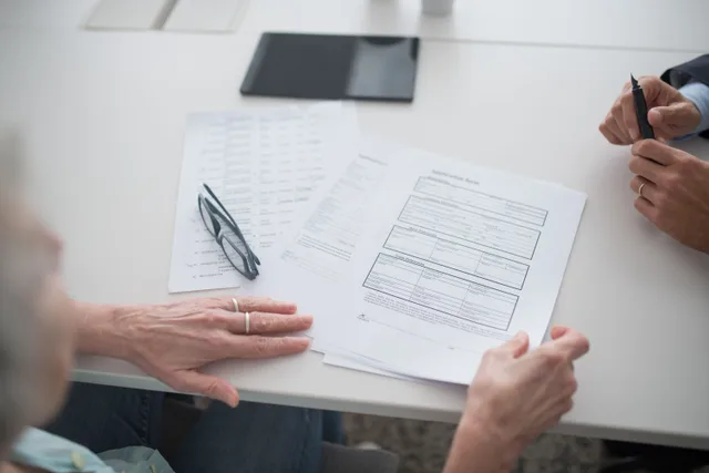 Close-up view of two individuals reviewing documents and forms in an office setting. Acquisition financing structures: SBA 7(a), seller notes, earnouts, mezzanine debt, and who carries risk