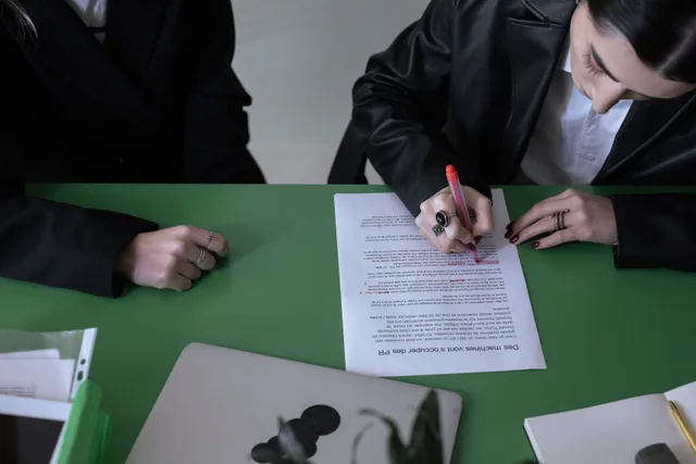 A woman marking a document with a red pen at a green desk. Acquisition financing rules worth knowing